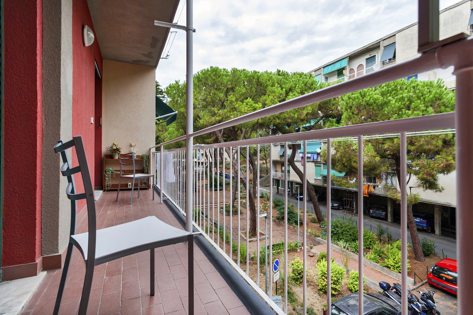 A balcony with metal railings overlooks trees and a street.