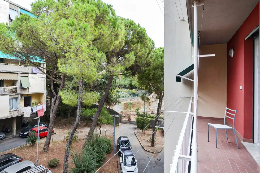 A balcony overlooks a tree-lined courtyard with nearby apartment buildings.