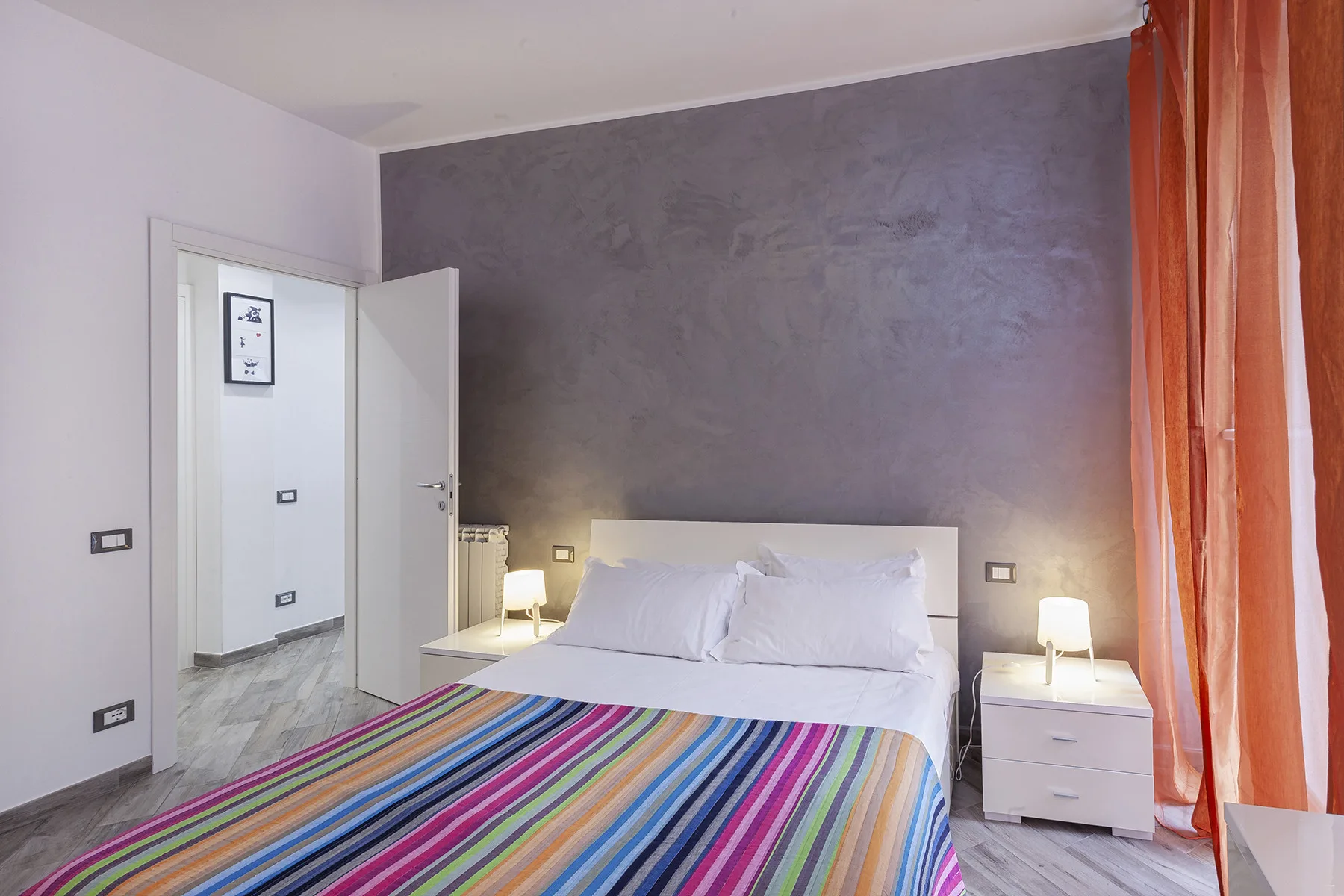 A bedroom with a bed covered by a colorful striped blanket.