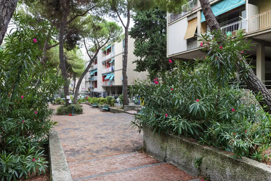 A paved courtyard walkway winds between apartment buildings and leafy shrubs.