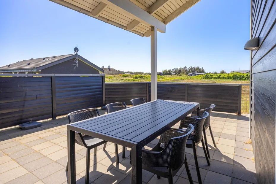 Un patio al aire libre con una mesa de comedor y asientos bajo un techo cubierto.