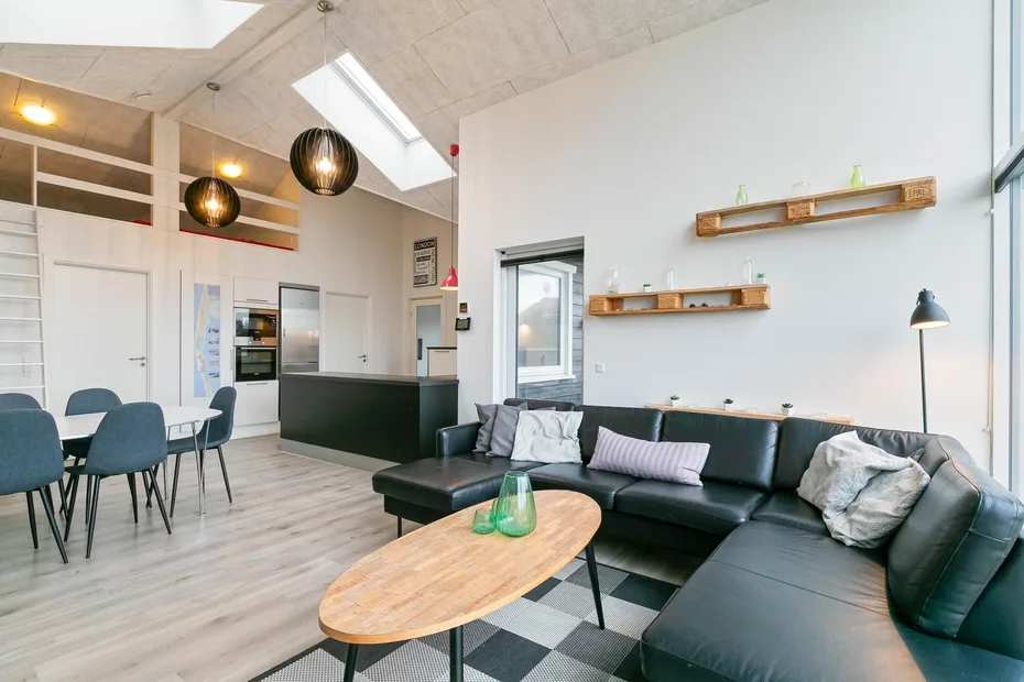 Una luminosa sala de estar y comedor de concepto abierto, con sofá seccional negro y mesa de centro de madera.