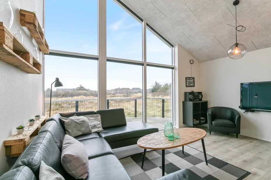 Una sala luminosa con grandes ventanas, asientos y una mesa de centro.