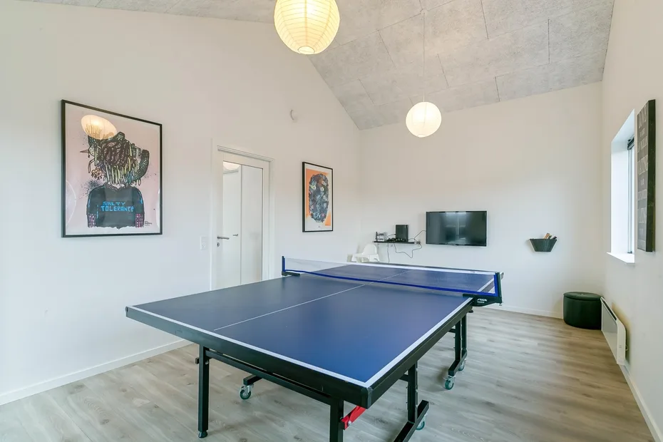 Una luminosa sala de recreación cuenta con una mesa de ping-pong y un televisor en la pared.