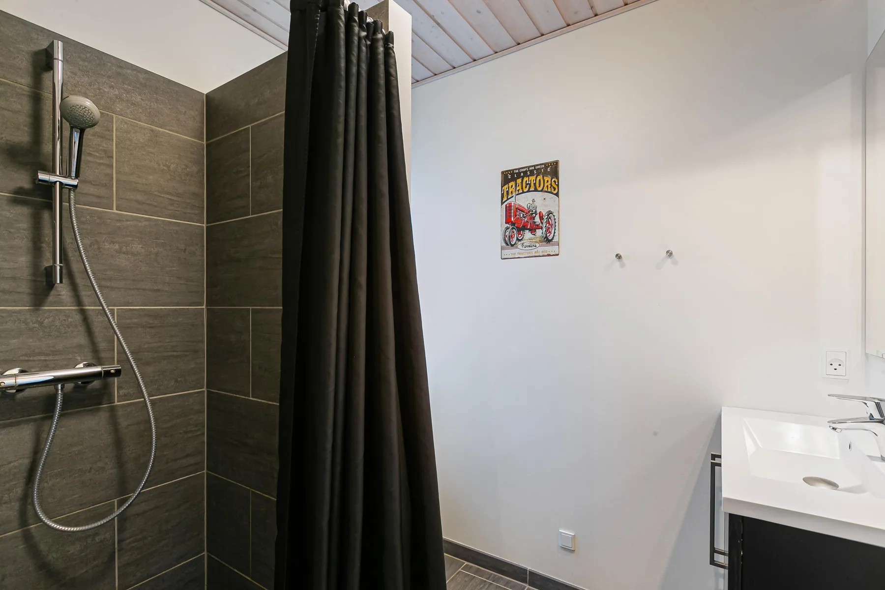 Un baño con una ducha tras una cortina oscura y un lavabo blanco.