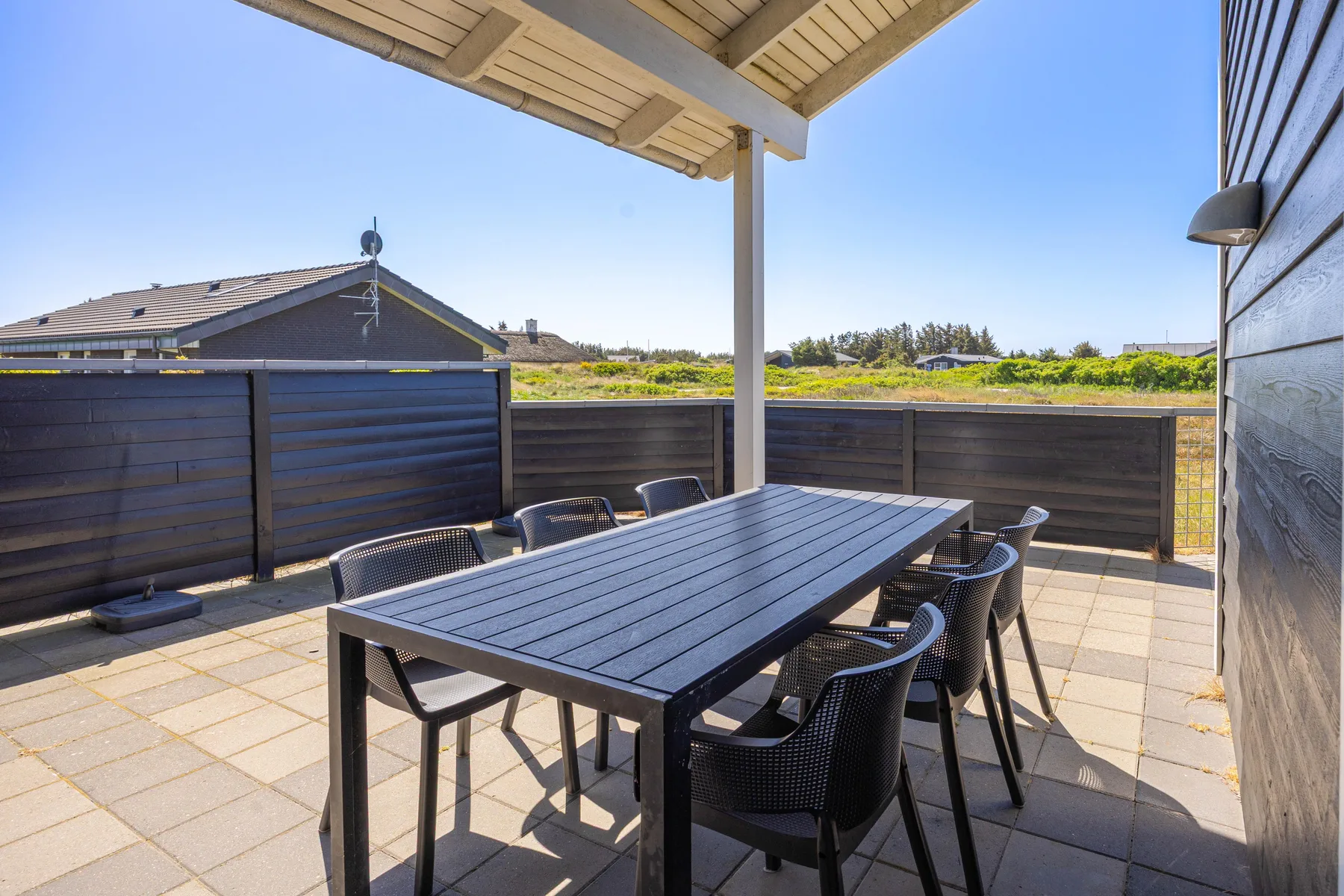 Una zona de comedor exterior cubierta tiene una mesa y asientos en un patio pavimentado.