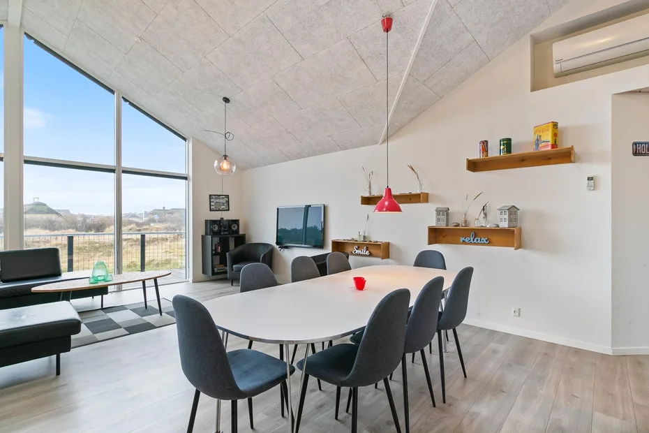 Un luminoso comedor y sala de estar tiene una mesa larga junto a grandes ventanas.