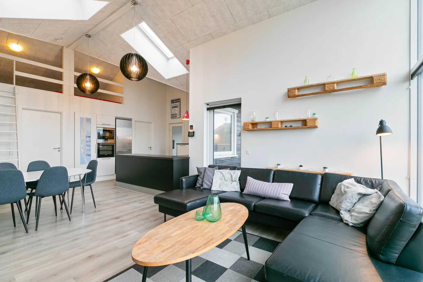 Una luminosa sala de estar diáfana con sofá seccional negro y zona de comedor.