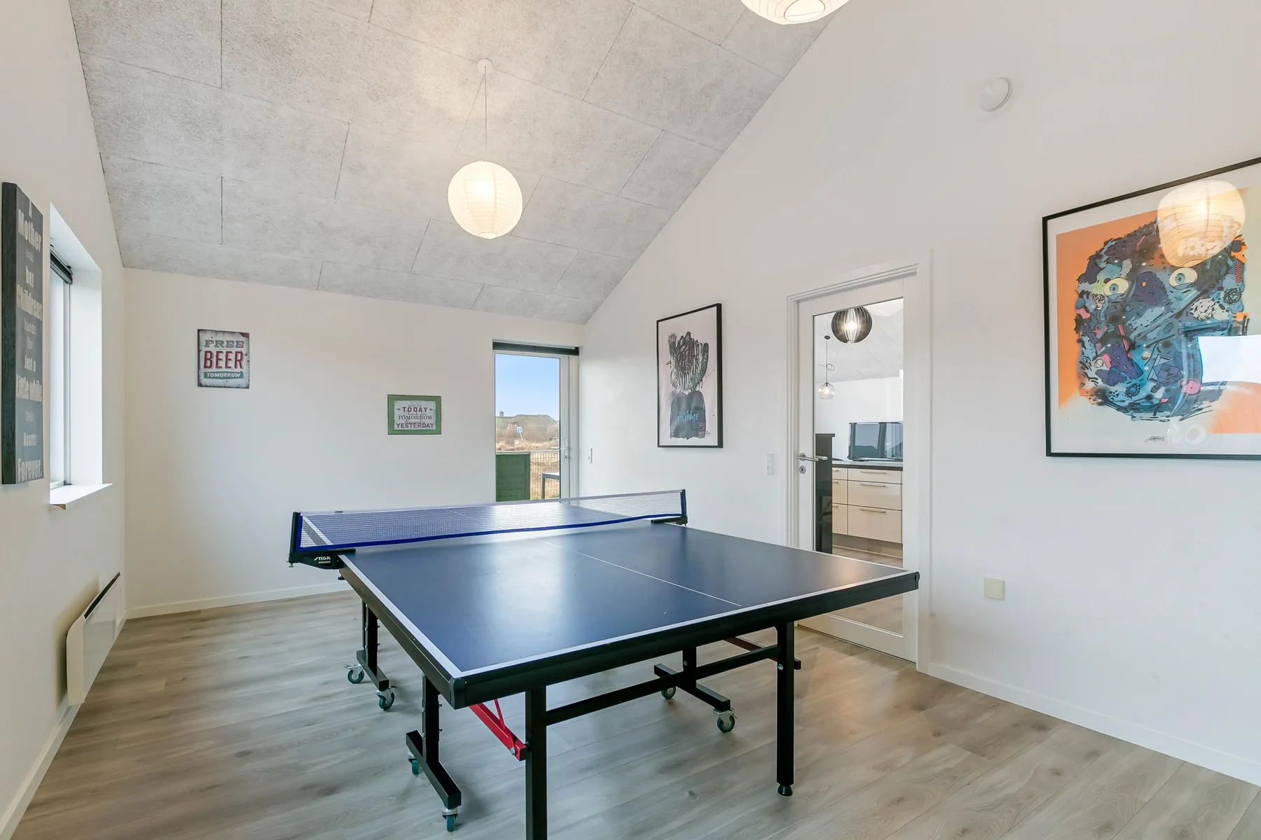 Una sala recreativa con una mesa de ping-pong azul y cuadros en las paredes.