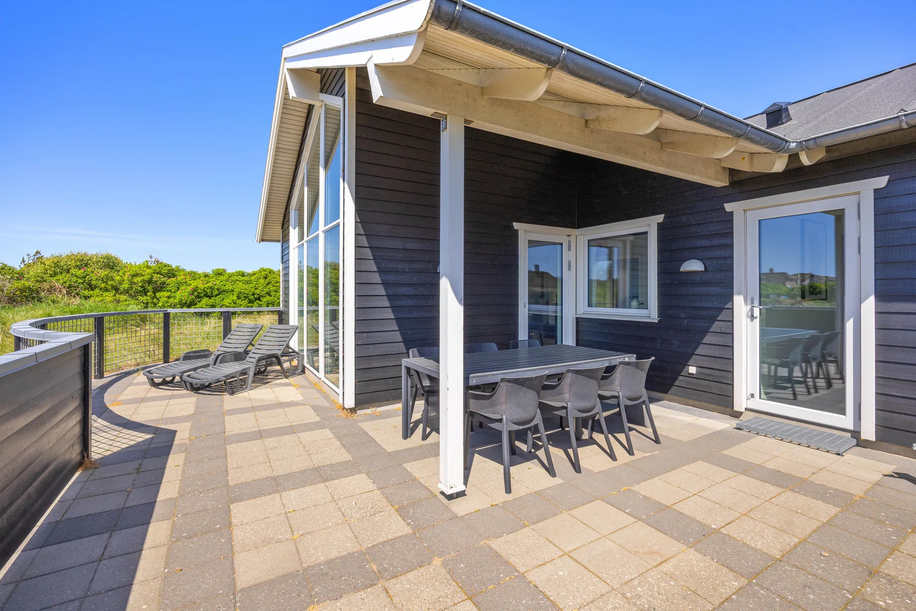 Un patio pavimentado con comedor exterior junto a una casa de revestimiento oscuro.