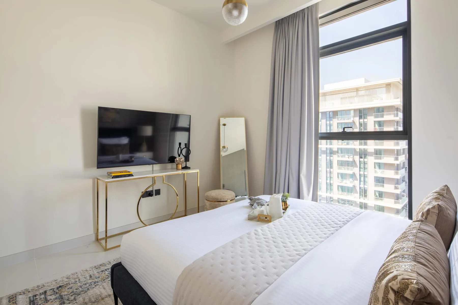 Un dormitorio con una cama bien tendida junto a una ventana grande y cortinas.