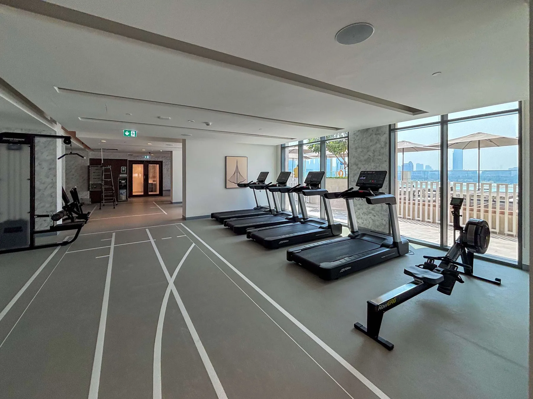 Una luminosa sala de ejercicio tiene cintas de correr y equipo junto a grandes ventanas.