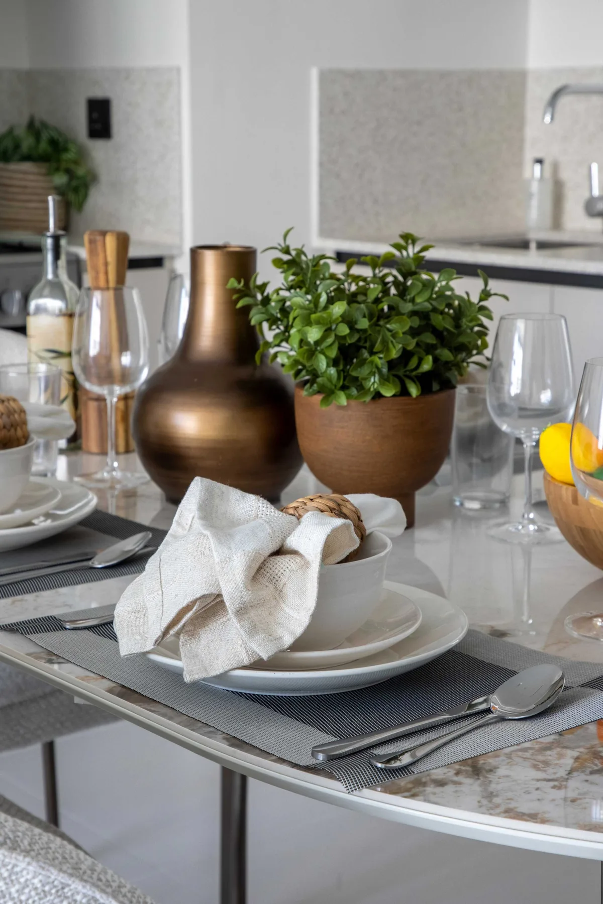 Una mesa de comedor está puesta con platos, cristalería y una planta en maceta.