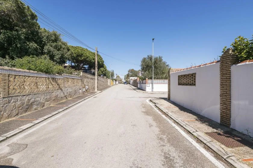 A quiet residential street lined with stone and white walls beneath a clear blue sky.