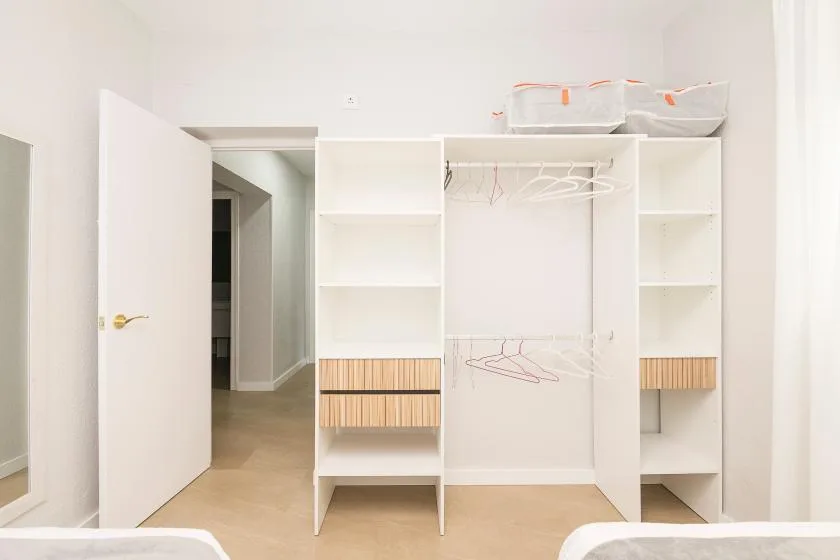 A white built-in wardrobe with open shelves, hanging rails, and drawers.