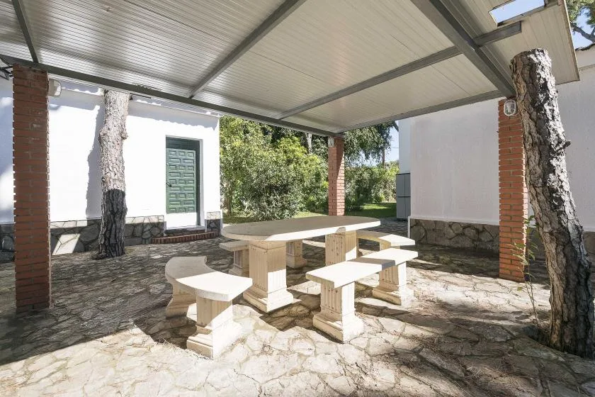 A covered outdoor dining area with a long table and stone paving.