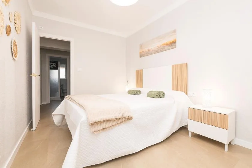 A bright bedroom with a neatly made bed and light wood accents.