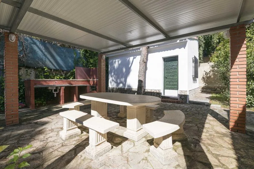 A covered outdoor dining area with a stone table and built-in benches.
