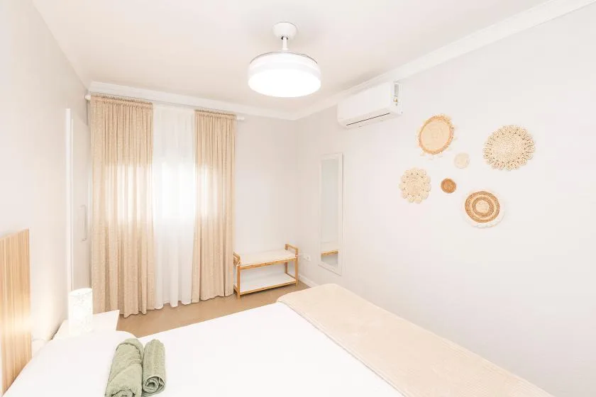 A bright bedroom with a bed, curtained windows, and woven wall decorations.