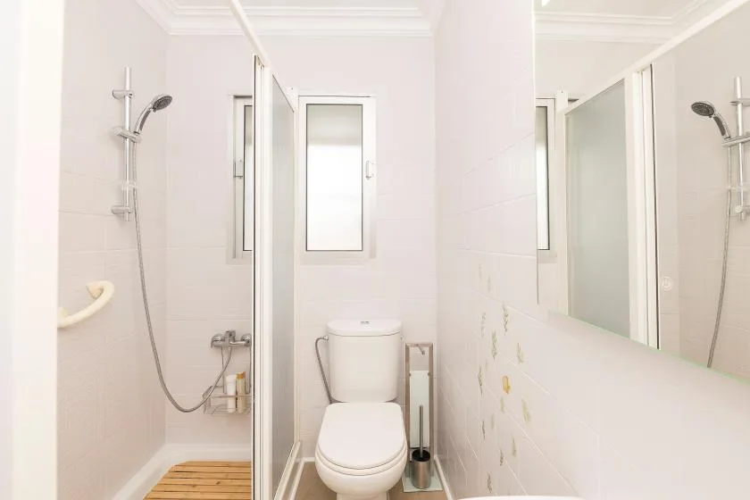 A bright bathroom with a toilet, shower, and small window.