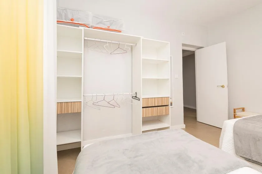 A bedroom with a bed beside an open wardrobe and an open door.