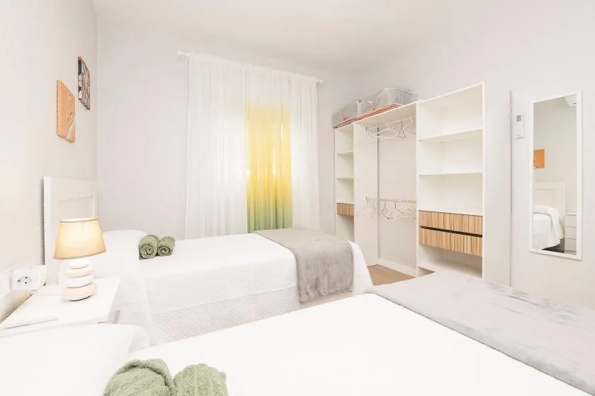 A bright bedroom with white bedding, a bedside lamp, and open shelving.