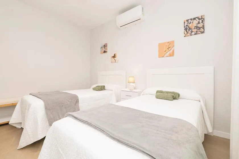 A bright bedroom with two beds, gray blankets, and small wall decorations.