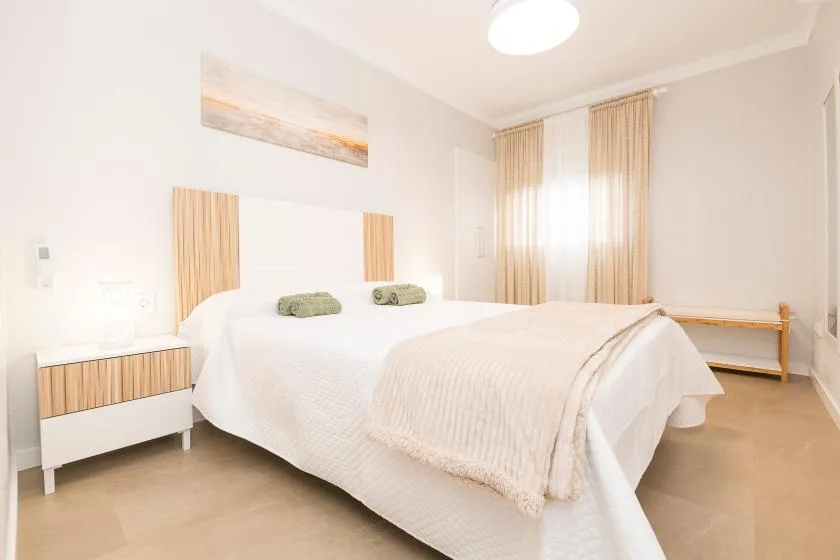 A bright bedroom with a white bed and tall curtained windows.
