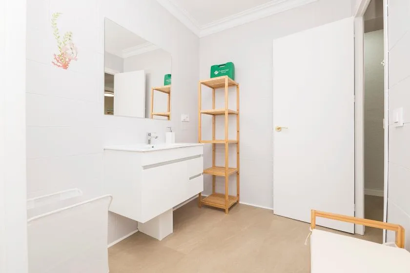 A bright bathroom with a white vanity, mirror, and open shelving.