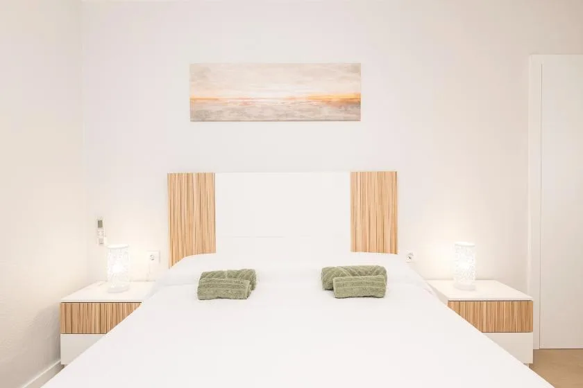 A bright bedroom with a neatly made bed and a landscape picture above it.