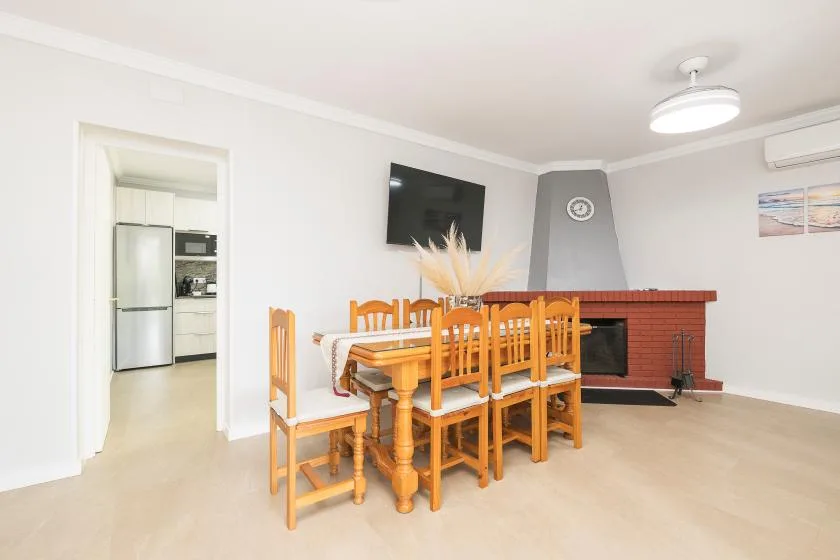 A dining area with a wooden table and chairs beside a living room fireplace.