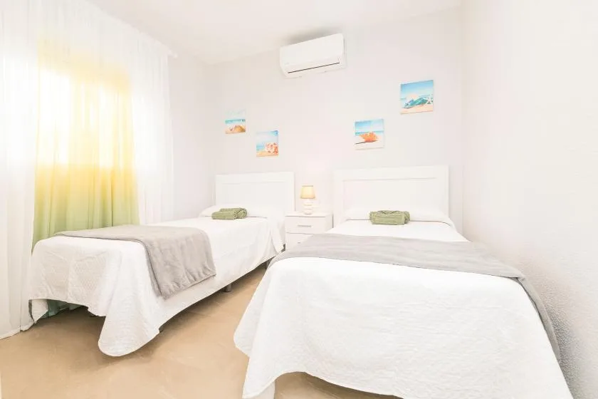 A bright bedroom with two beds and a window with sheer curtains.