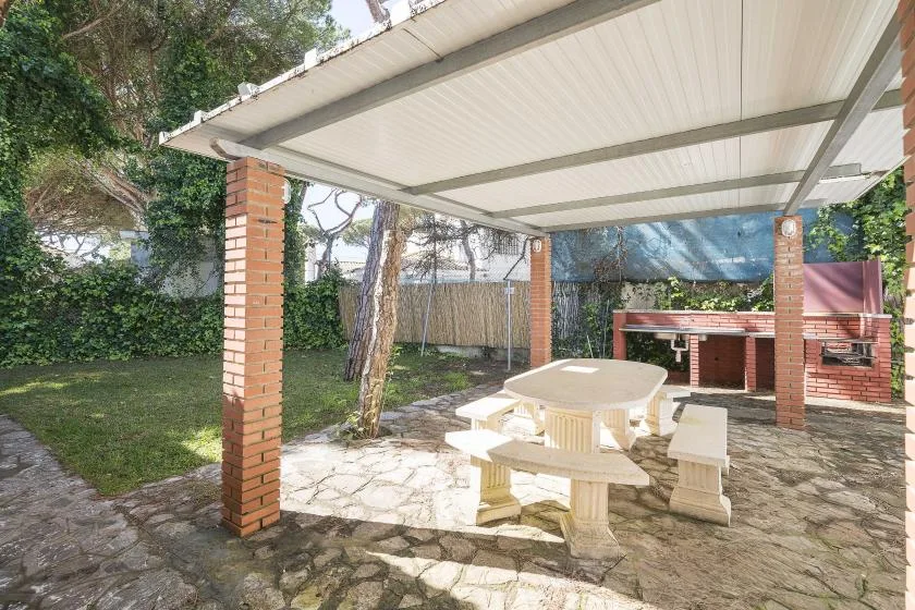 A covered outdoor patio with a picnic table and a brick barbecue.