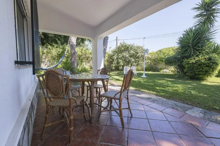 A covered patio with a round table and chairs overlooks a green garden.