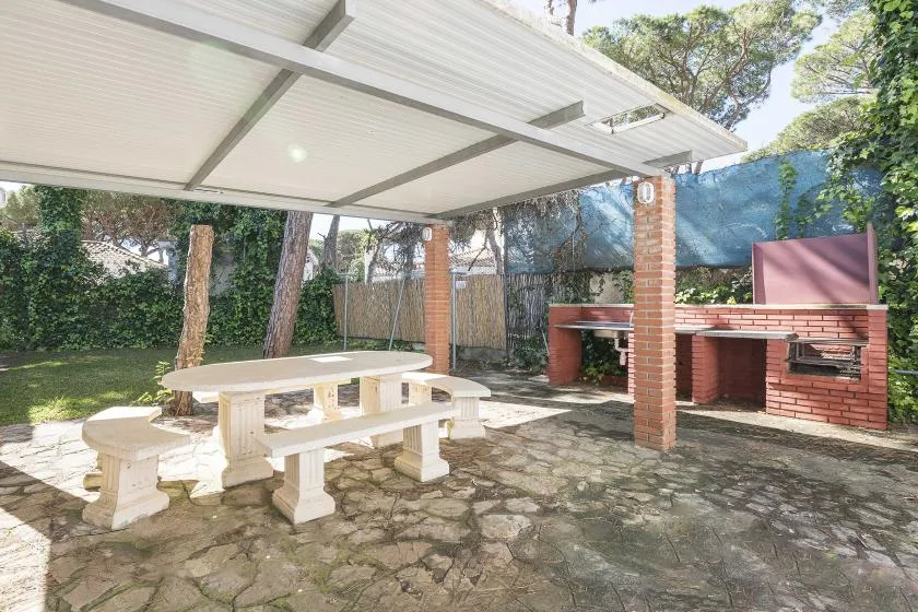 A covered outdoor dining area with picnic seating and a brick barbecue.