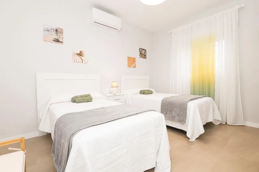 A bright bedroom with two beds dressed in white linens.