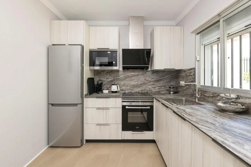 A bright modern kitchen with light cabinets, stainless appliances, and a long countertop.