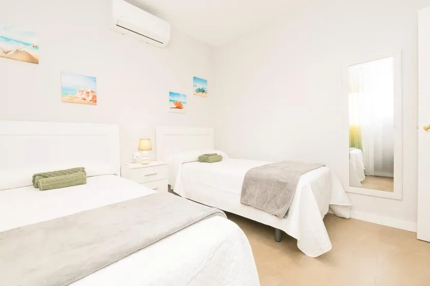 A bright bedroom with two beds, white bedding, and beach-themed wall art.