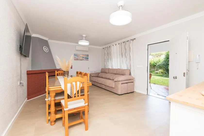 A bright living and dining area with a table, seating, and an open exterior door.
