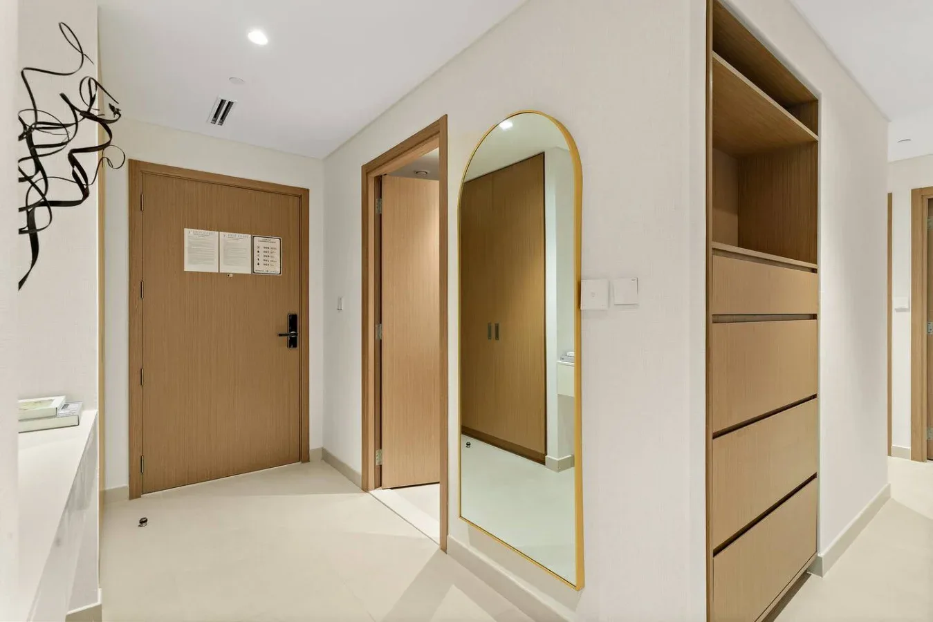 A bright entryway with a wooden door, an arched mirror, and built-in storage.