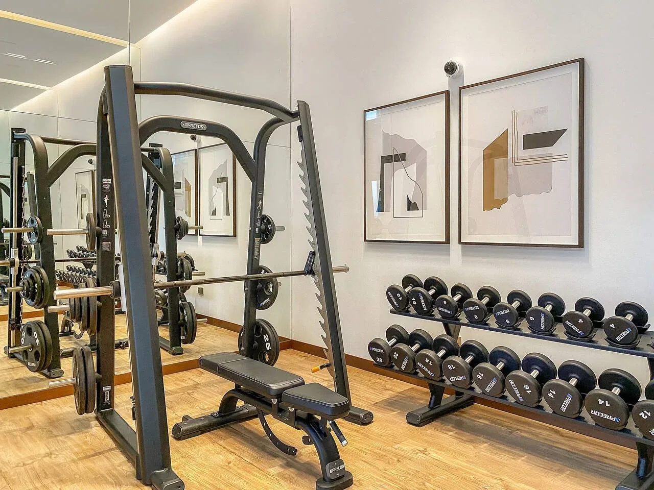 A gym with weight machines, a bench, and dumbbells beneath framed artwork.
