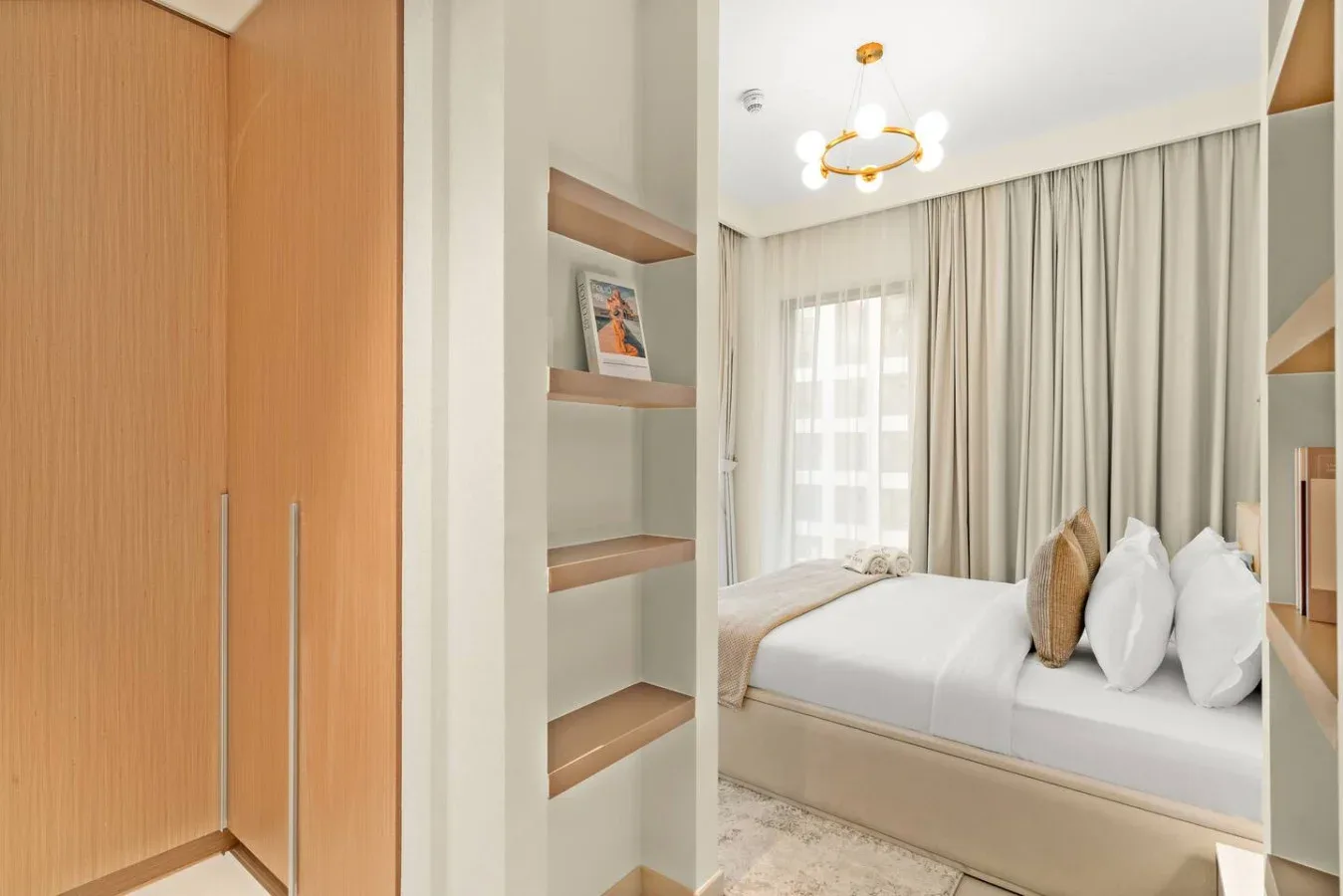 A bedroom with a neatly made bed beside built-in shelving.