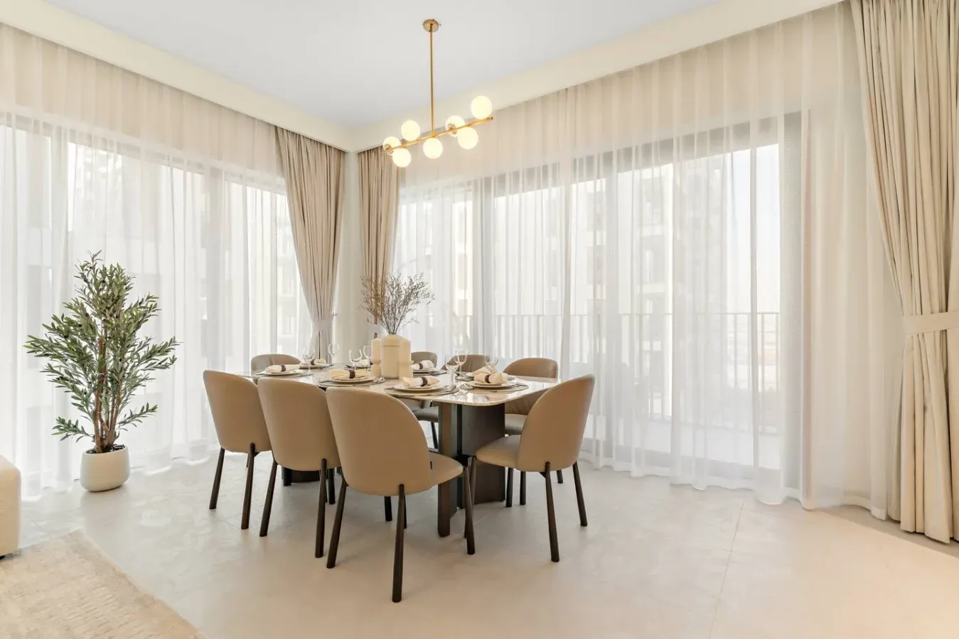 Dining area with a set table beside large windows with sheer curtains.
