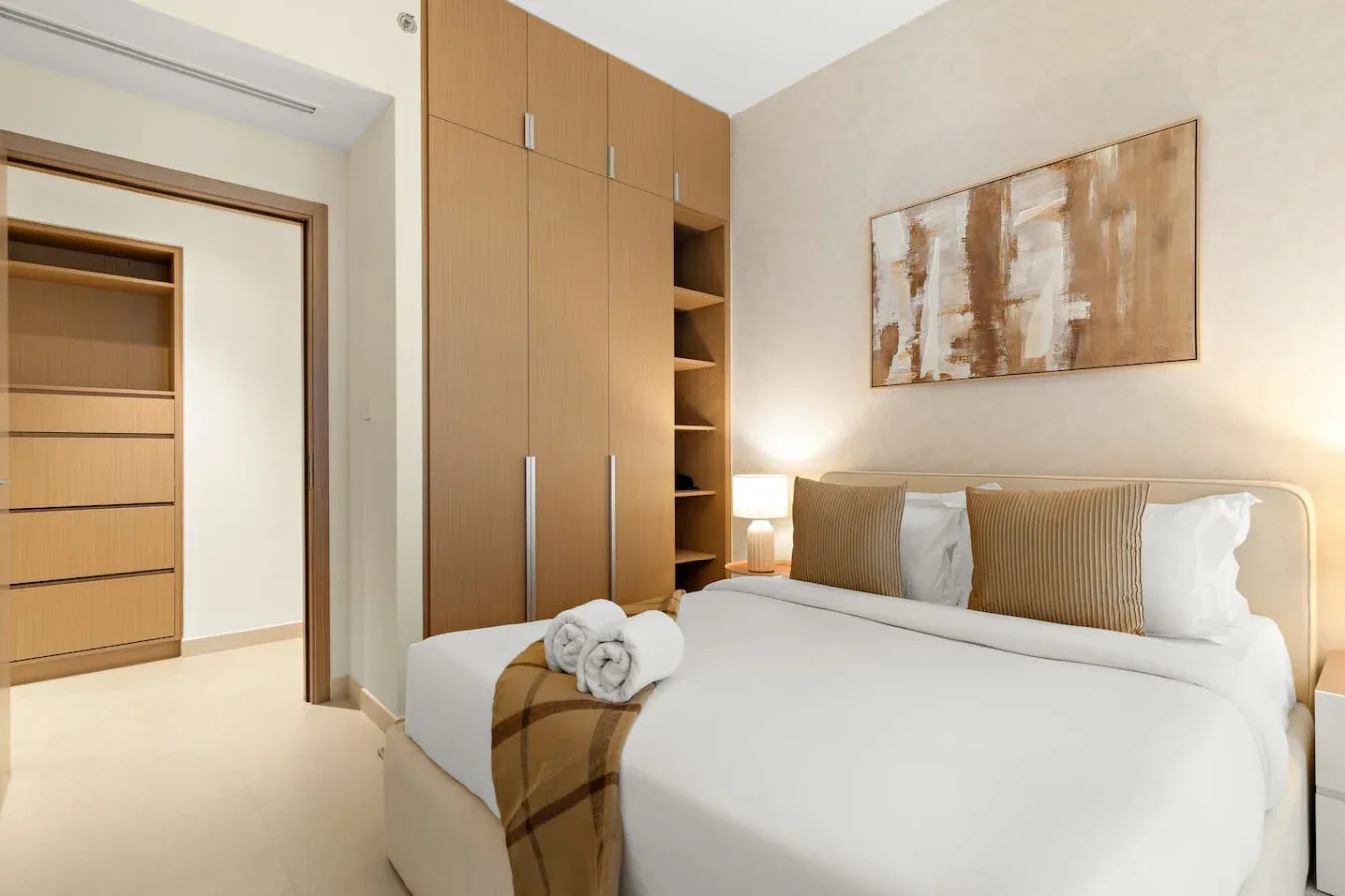 A bright bedroom with a neatly made bed and built-in wooden storage.
