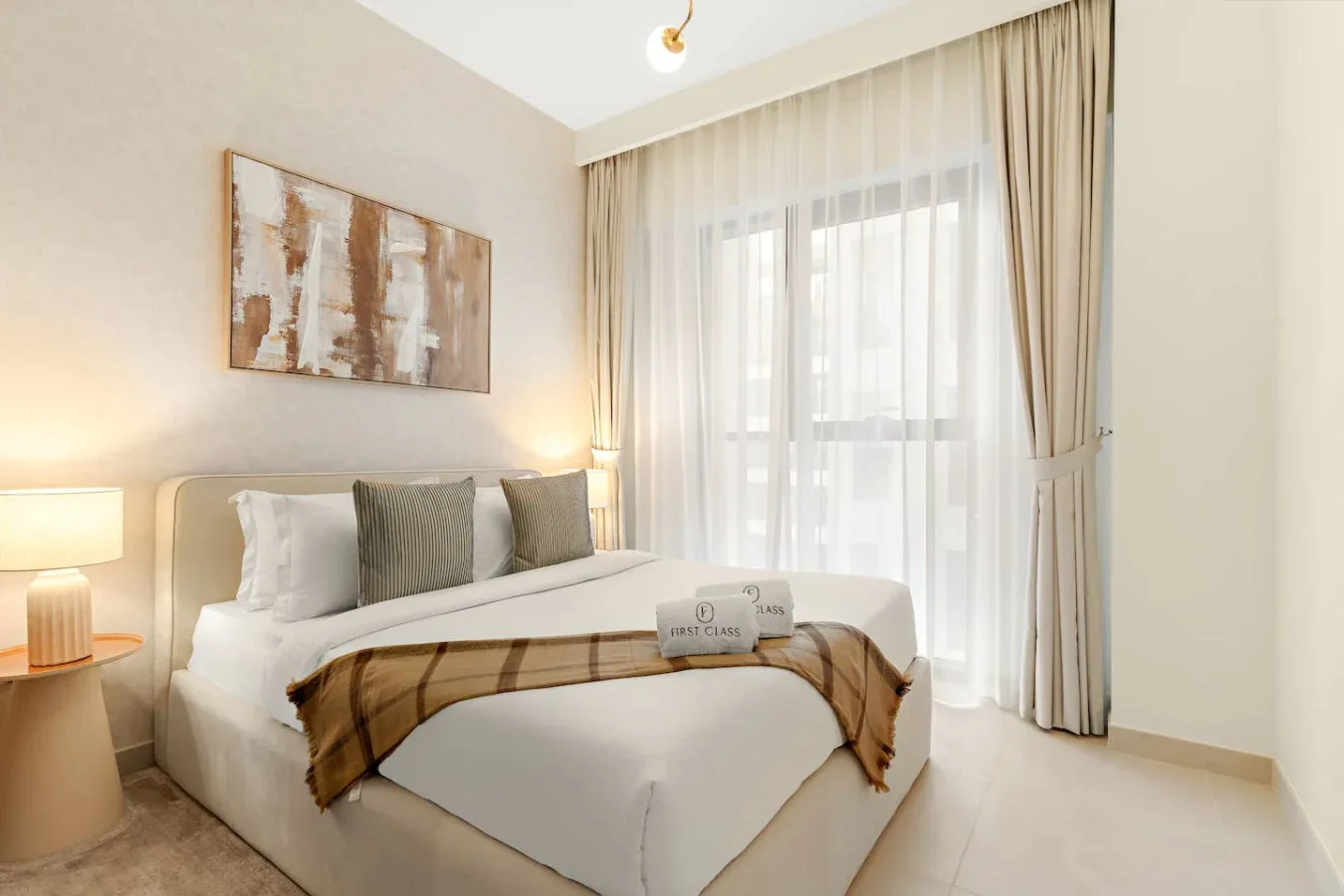 A bright bedroom with a neatly made bed and tall curtained windows.