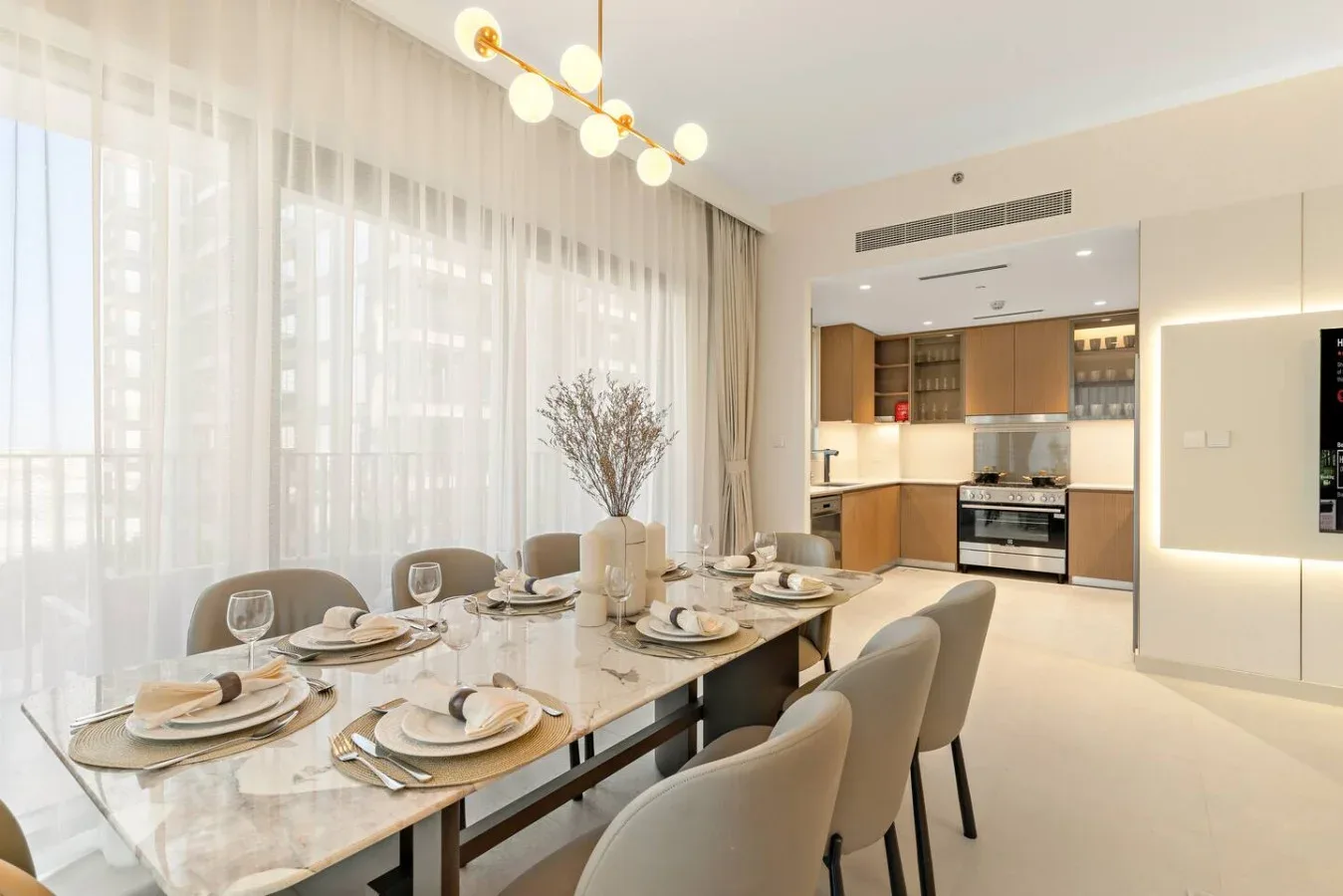 A bright dining area with a set table beside large curtained windows.