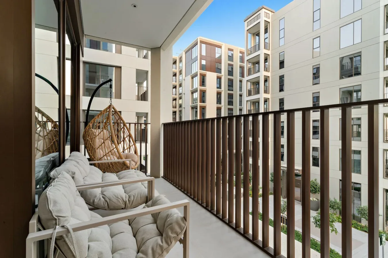 A balcony with cushioned seating and a hanging chair overlooks nearby apartment buildings.