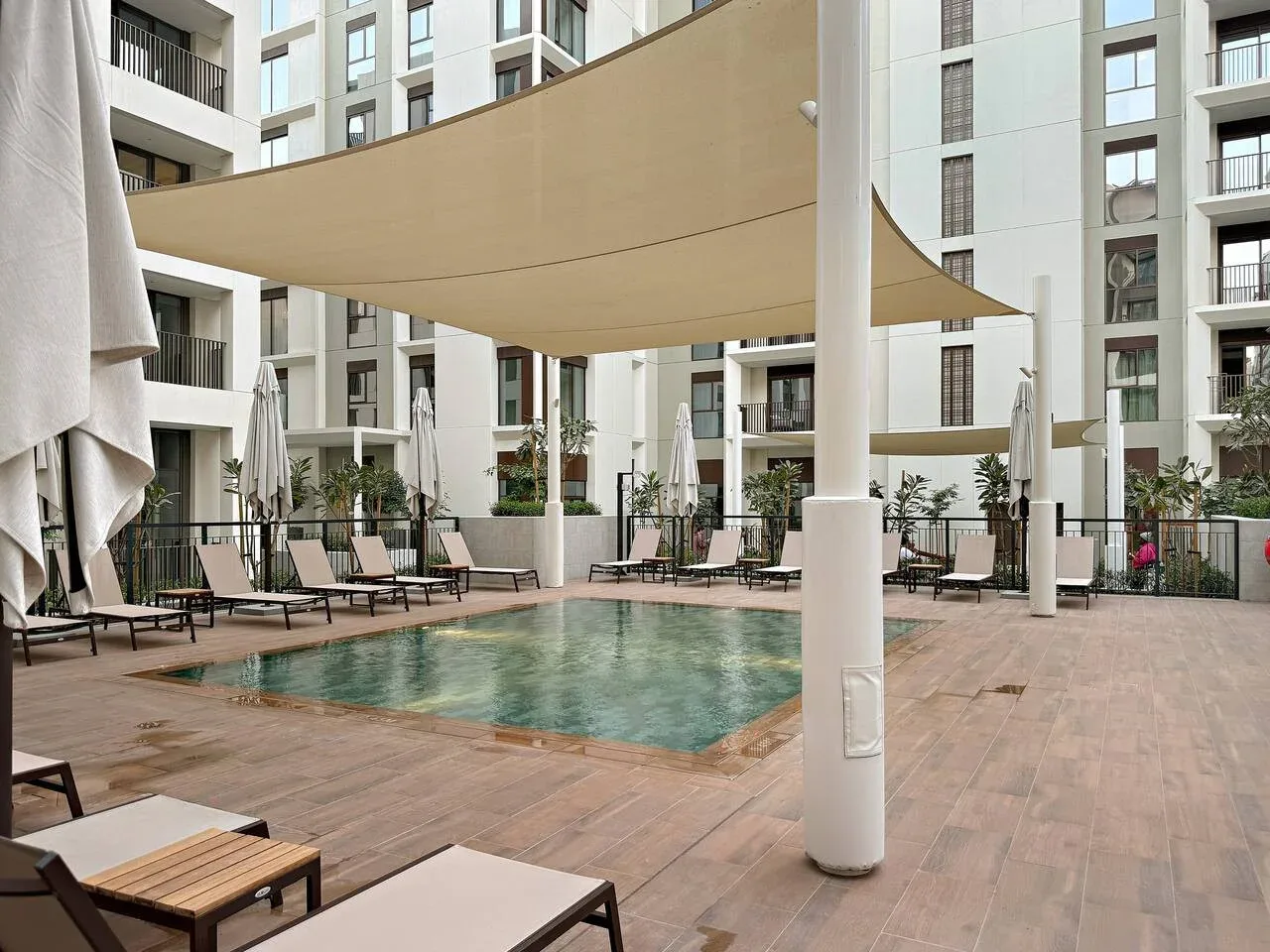 An outdoor pool surrounded by lounge seating beneath large shade canopies.