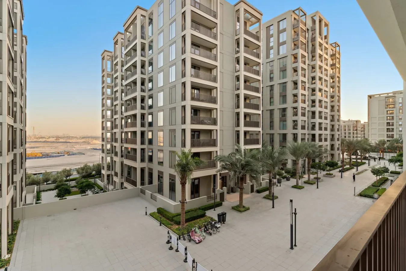 A paved courtyard runs between modern apartment buildings, with palm trees and outdoor seating.