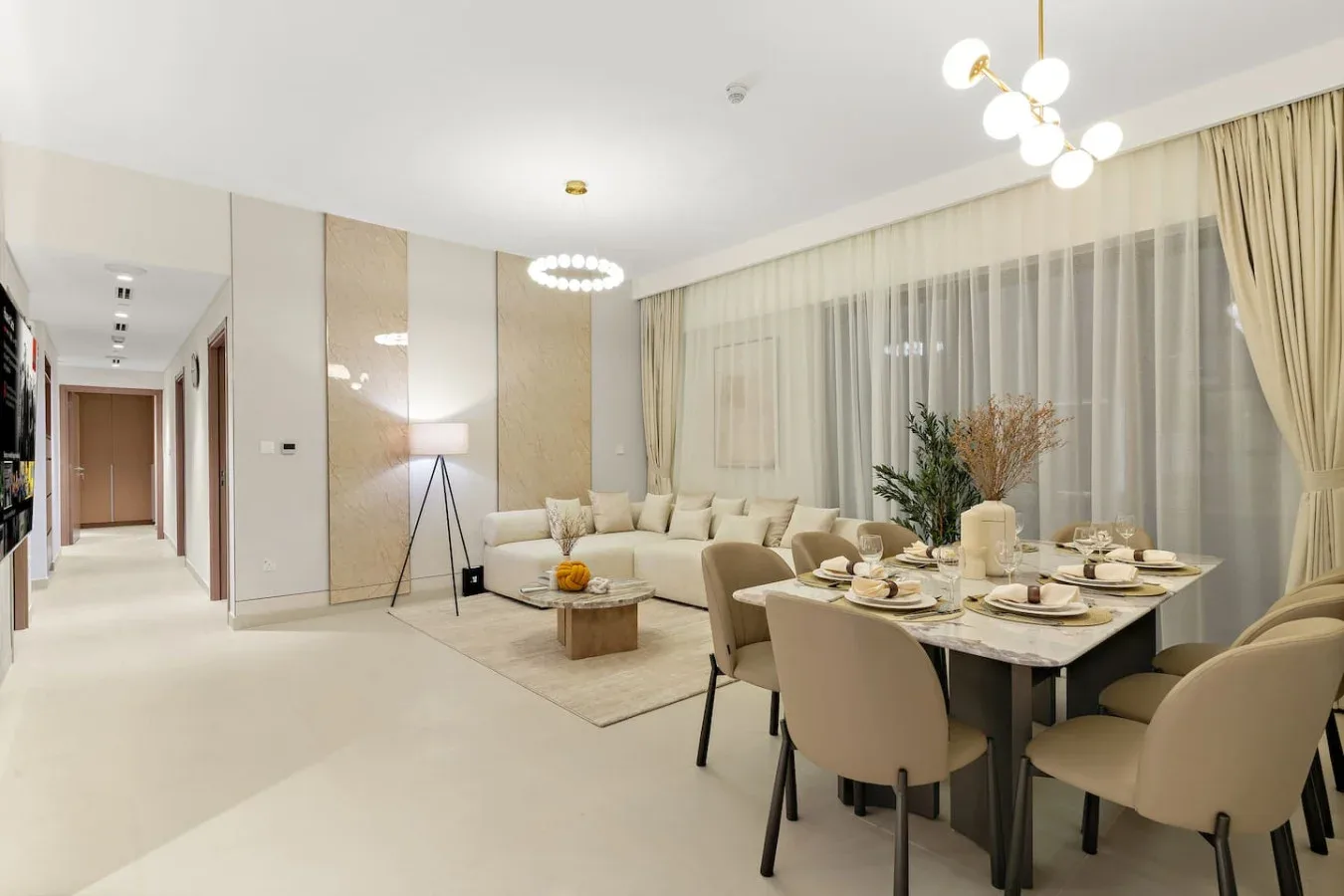 A bright living and dining area with seating, a dining table, and large curtained windows.
